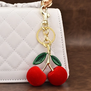 Furry red cherry keychain with green glitter leaves and golden clasp on white bag