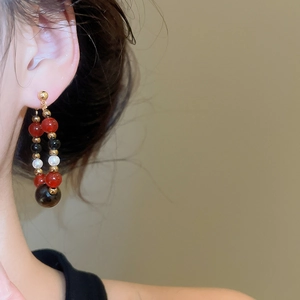 Detailed view of beaded hoop earrings with red, black, and white pearls on a female model