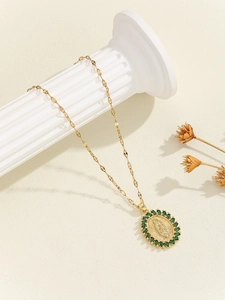 Close-up of gold Virgin Mary necklace with green cubic zirconia on a white pedestal