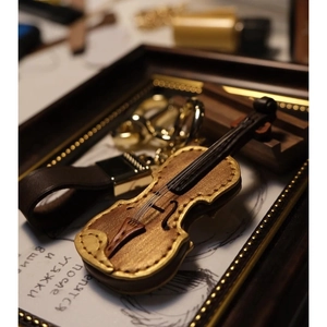Brown leather violin keychain with golden accents and metal ring on vintage desk