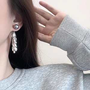 Detail of silver long tassel earrings with leaf-shaped metal scales and grey bead on model