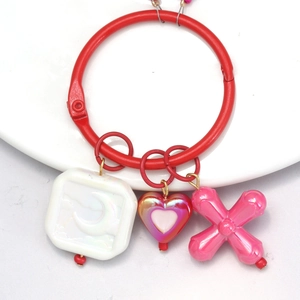 Detail of red loose-leaf ring with moon, heart, and cross charms on a white background