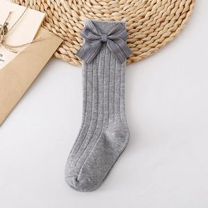 Detail of grey knitted children socks with decorative glitter dark grey bow on white desk