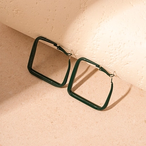 Detailed view of dark green square geometric earrings on a minimalist orange pedestal