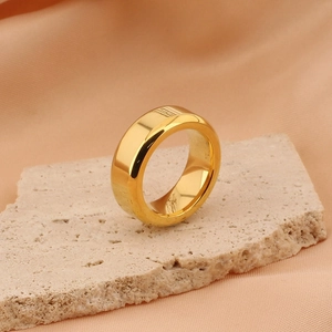 Polished gold titanium steel wide band ring displayed on natural beige stone