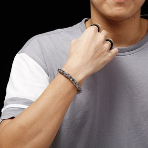 Close-up of silver Byzantine chain bracelet and fashion rings on male model's wrist