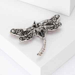 Detail of silver dragonfly brooch featuring yellow and red gemstone wings on a white stand