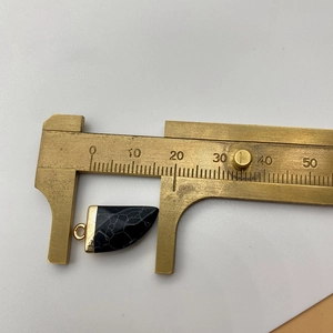 Macro shot of 19mm black stone chili pendant with gold caps measured by brass caliper