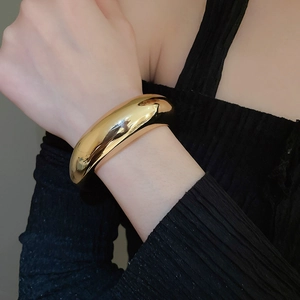 Close-up of a wide gold cuff bracelet with high-polish mirror finish on a model's wrist