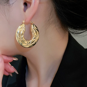 Detail of golden hoop earring with geometric lattice texture on female model ear