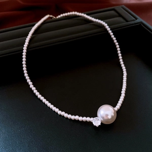 Detail view of pearl necklace with large round pearl and sparkling diamond on black tray