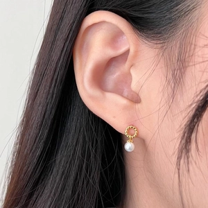 Macro shot of 925 silver twist hoop earrings with white pearls on a model's ear