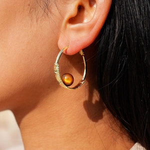 Close-up of golden textured hoop earring with a brown bead worn by a model