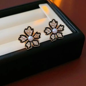 Makroaufnahme von Blumenohrringen mit schwarzer Emaille, Kristallen und Perle