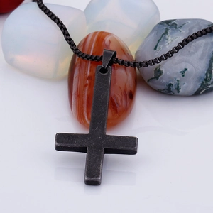 Macro shot of retro black cross pendant with round bead chain on natural stones