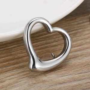 Polished heart-shaped hollow metal pendant on wooden background for DIY necklace making