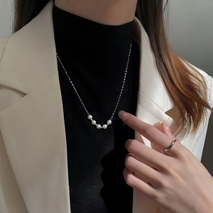 Detail of five white pearls on a silver chain necklace worn with a minimalist silver ring
