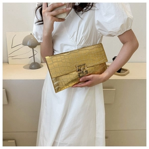 Detail of gold faux leather clutch with crocodile texture held by a model in a white dress