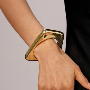 Polished gold irregular geometric cuff bracelet on a model wearing black clothing