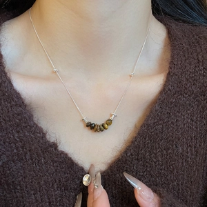 Close-up of tiger eye stone pendant on silver chain necklace worn over a brown sweater