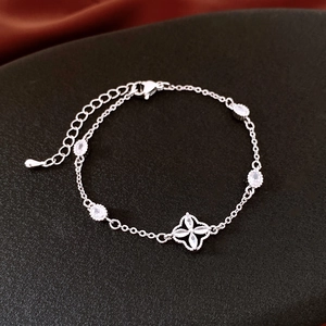 Detailed view of a silver clover bracelet with white zircons on a textured black base