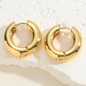 Macro detail of chunky gold hoop earrings on textured white stone background