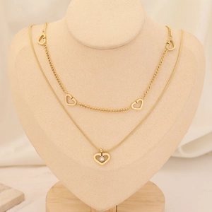 Detail of gold double layer necklace with heart cutouts and heart pendant with gem