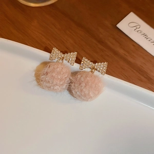 Detail of a gold ribbon stud earring with a soft pink plush ball on a ceramic tray