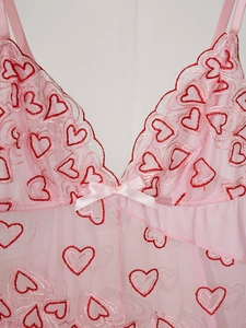 Détail de nuisette en résille rose avec broderies de cœurs rouges et nœud sur le décolleté