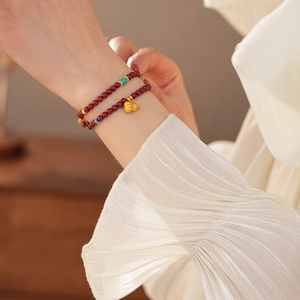 Detail of double-layer cinnabar bead bracelet with golden pumpkin charm on model wrist