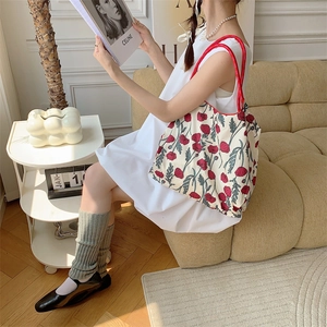 Detail shot of a floral canvas tote bag featuring red flower prints and red round handles