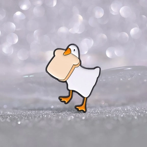 Detailed view of creative white goose enamel pin with bread on metallic bokeh background