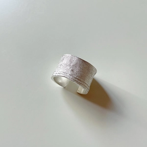 Close-up of silver ring with wide band and irregular beaded texture in minimalist style