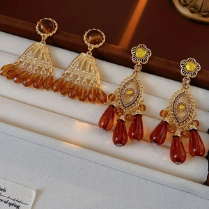 Detail of vintage gold earrings with tiger eye beads and rhinestones on a white stand