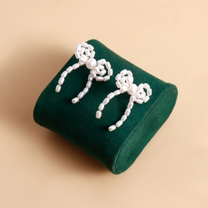 Macro detail of handmade woven pearl bow earrings on a vintage green velvet stand