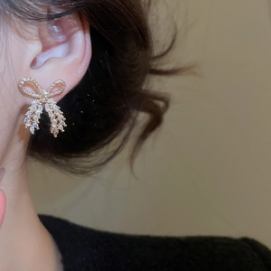 Detail of elegant gold bow earrings with sparkling cubic zirconia worn by model