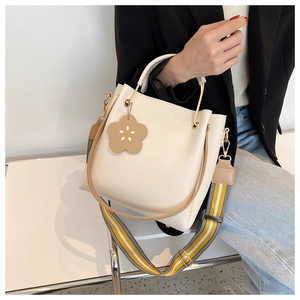 Detail der cremeweißen Beuteltasche mit Leder-Blumenanhänger und buntem Gurtband