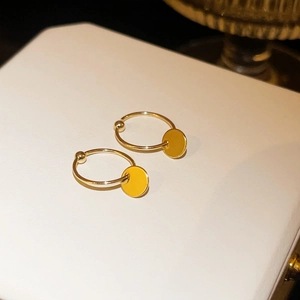 Detail view of golden hoop earrings with round pendant on white textured pedestal