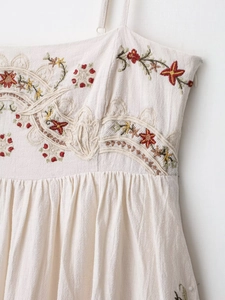 Close-up of colorful floral embroidery and textured cotton-linen fabric on off-white dress