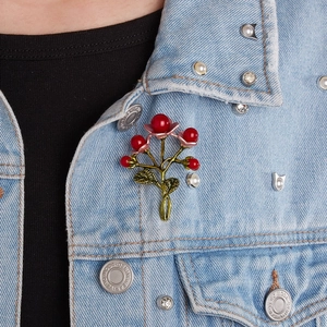 Detailed close-up of a berry brooch with red beads and green leaves on denim jacket