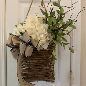 Close-up of artificial hydrangea basket hanging on white door with burlap bow detail