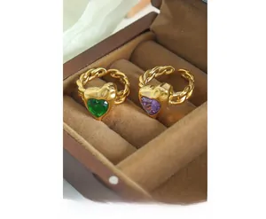 Macro detail of gold plated heart rings with purple and green crystals in a wooden box