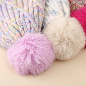 Nahaufnahme von flauschigen Kunstfell-Pompons an bunten Strickmützen für Mädchen