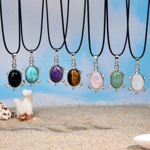Plusieurs colliers tortue avec pendentifs en pierre naturelle sur fond de plage