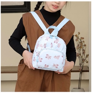 Detail of light blue cartoon bear print backpack with front zipper pocket and straps