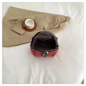 Detail view of red rivet shell bag with metal frame clasp and brown fabric lining