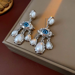 Detail of vintage silver earrings with blue eye motif and dangling pearls on jewelry box