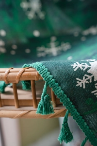 Close-up of dark green knitted blanket with white snowflake patterns and fringe trim