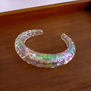Macro view of a colorful iridescent resin open cuff bangle with textured wave ripples