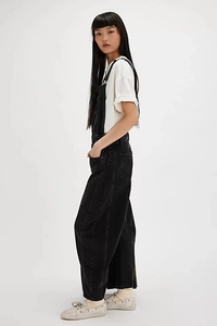 Side view of retro washed loose denim overalls paired with a white t-shirt and flat shoes